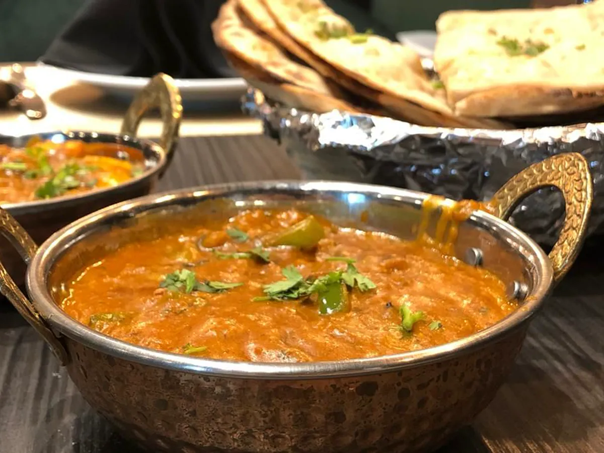 Butter chicken in a karahi with a basket of naan